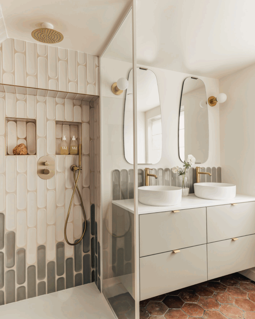 Salle de bain contemporaine renovée avec meuble Bocklip en finition vert tige satiné, double vasque ronde, miroirs graphiques et douche à l’italienne carrelée en relief beige et gris.