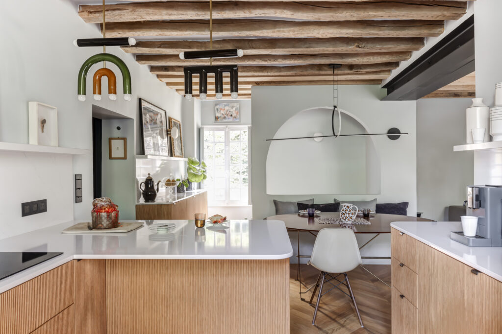 Cuisine ouverte Bocklip en chêne naturel plissé avec îlot central et coin repas convivial, poutres apparentes et suspension design.
